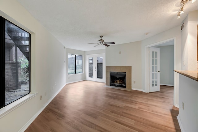 unfurnished living room featuring a tiled fireplace, ceiling fan, light hardwood / wood-style floors, a textured ceiling, and french doors