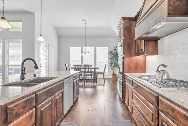 kitchen with dark wood-type flooring, hanging light fixtures, light stone countertops, custom range hood, and stainless steel appliances