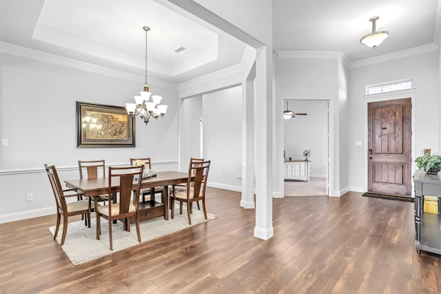 dining area featuring ornamental molding, ceiling fan with notable chandelier, a tray ceiling, and dark wood-type flooring