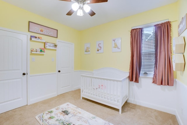 carpeted bedroom featuring ceiling fan and a nursery area