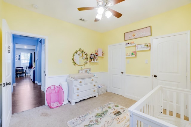 carpeted bedroom with a crib and ceiling fan