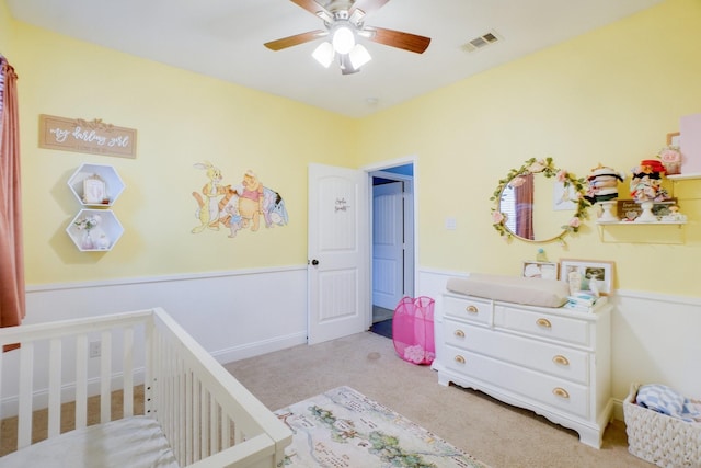 carpeted bedroom featuring a crib and ceiling fan