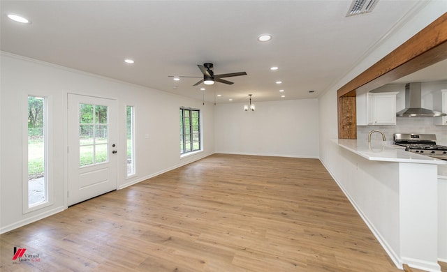 unfurnished living room with ceiling fan with notable chandelier, light hardwood / wood-style flooring, and crown molding