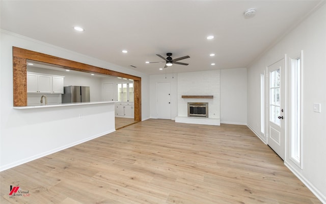 unfurnished living room featuring sink, light hardwood / wood-style flooring, ceiling fan, ornamental molding, and a fireplace