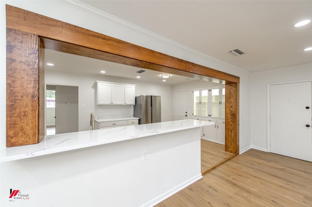 kitchen featuring stainless steel refrigerator, white cabinetry, light stone countertops, kitchen peninsula, and light wood-type flooring