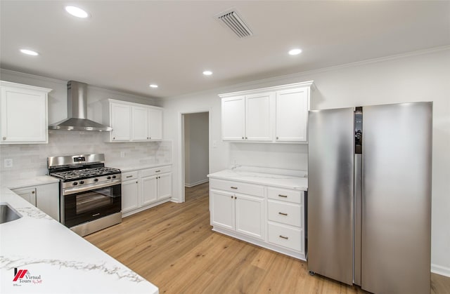 kitchen with light wood-type flooring, tasteful backsplash, stainless steel appliances, wall chimney range hood, and white cabinets