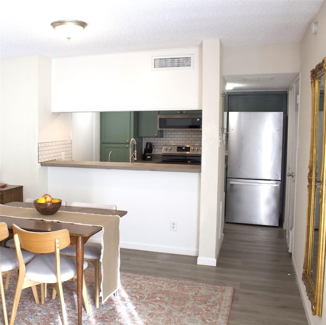 kitchen with a textured ceiling, kitchen peninsula, dark wood-type flooring, and appliances with stainless steel finishes