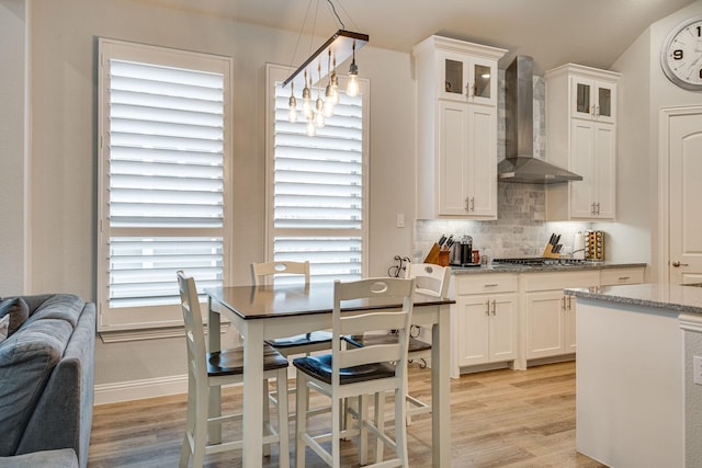 kitchen featuring white cabinetry, hanging light fixtures, wall chimney range hood, light stone counters, and light hardwood / wood-style floors