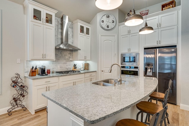 kitchen with a center island with sink, sink, wall chimney exhaust hood, appliances with stainless steel finishes, and decorative light fixtures