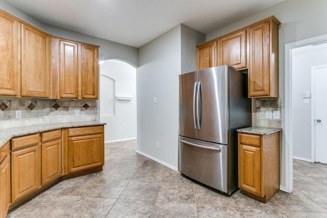 kitchen with tasteful backsplash, stainless steel refrigerator, light stone countertops, and light tile patterned floors