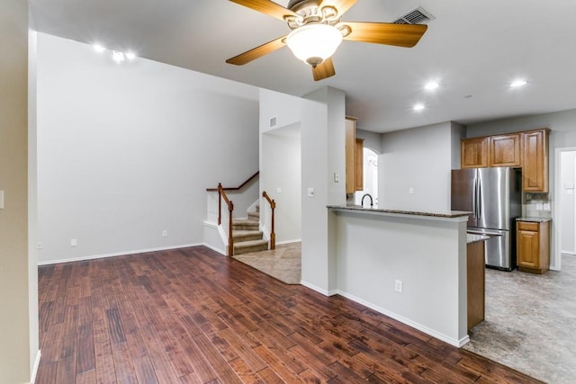 kitchen with dark wood-type flooring, ceiling fan, stainless steel fridge, decorative backsplash, and kitchen peninsula