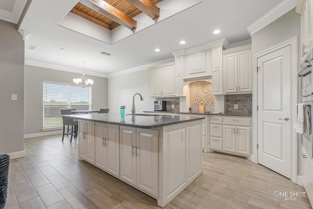 kitchen with sink, white cabinetry, a center island with sink, dark stone counters, and backsplash