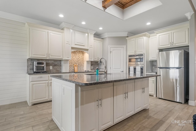 kitchen with appliances with stainless steel finishes, sink, a kitchen island with sink, and dark stone countertops