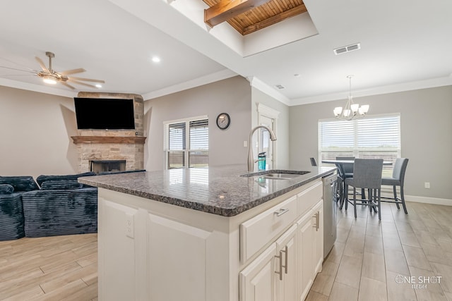 kitchen with stainless steel dishwasher, ceiling fan with notable chandelier, sink, a center island with sink, and a fireplace