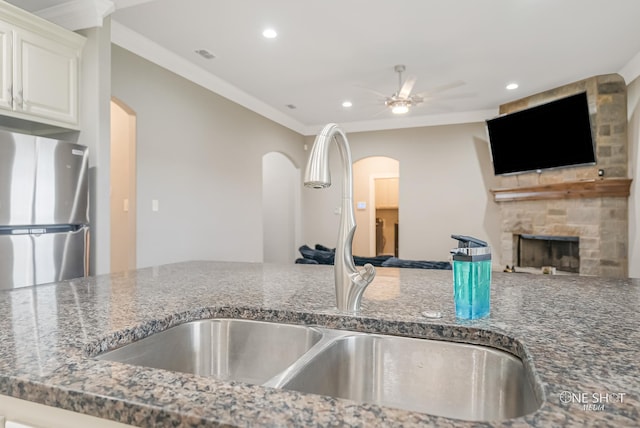 kitchen with sink, crown molding, stainless steel refrigerator, a fireplace, and white cabinets