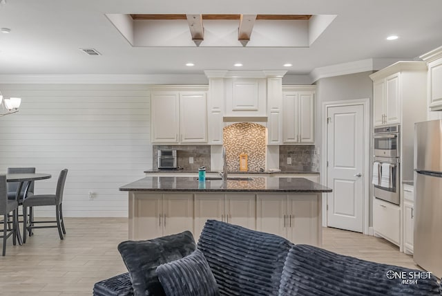 kitchen featuring backsplash, dark stone counters, an island with sink, and appliances with stainless steel finishes