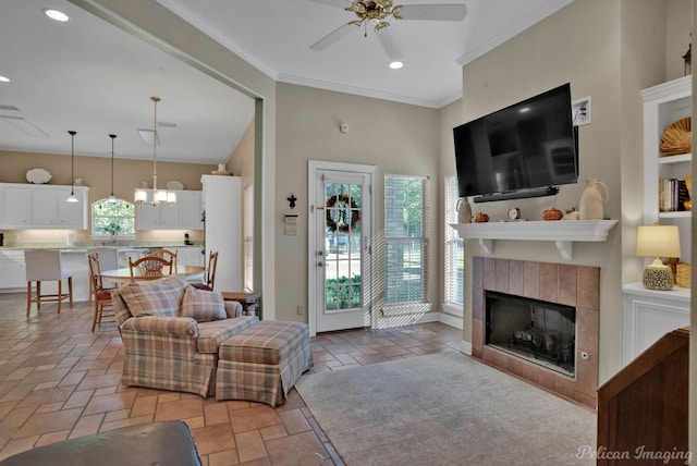 living room featuring a towering ceiling, ornamental molding, ceiling fan with notable chandelier, and a tile fireplace