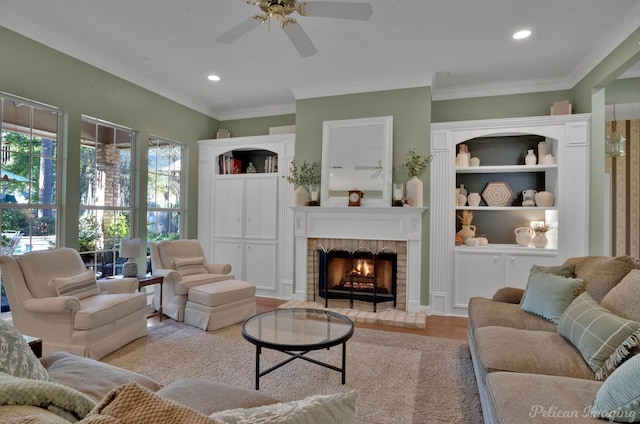 living room featuring crown molding, ceiling fan, a fireplace, and light hardwood / wood-style floors