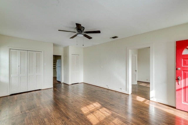 unfurnished bedroom with multiple closets, ceiling fan, white fridge, and dark wood-type flooring