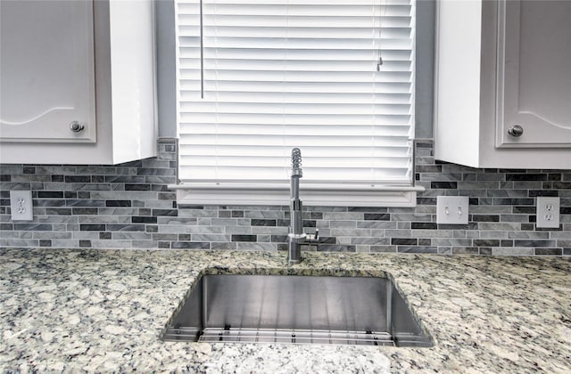 room details featuring backsplash, light stone counters, and sink