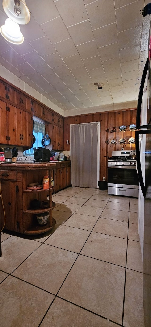 kitchen with light tile patterned floors, refrigerator, stainless steel stove, and wood walls