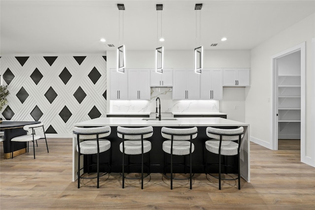 kitchen featuring a kitchen island with sink, sink, decorative light fixtures, and light wood-type flooring