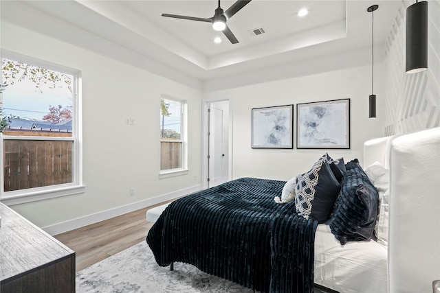 bedroom with a raised ceiling, ceiling fan, and light wood-type flooring