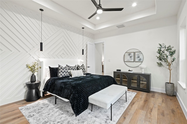 bedroom with hardwood / wood-style flooring, a raised ceiling, and ceiling fan