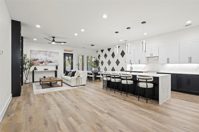 kitchen with ceiling fan, hanging light fixtures, an island with sink, light hardwood / wood-style floors, and decorative backsplash