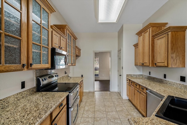 kitchen featuring light tile patterned flooring, stainless steel appliances, sink, and light stone counters