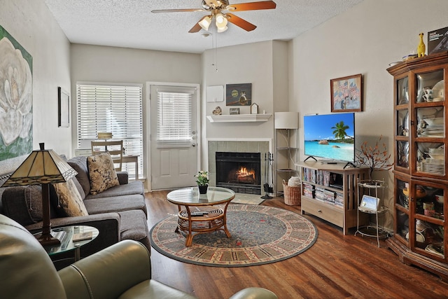 living room featuring ceiling fan, a fireplace, dark hardwood / wood-style flooring, and a textured ceiling