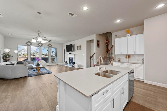 kitchen featuring white cabinetry, a kitchen island with sink, sink, and hanging light fixtures