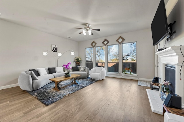 living room with a tile fireplace, ceiling fan, and light hardwood / wood-style floors