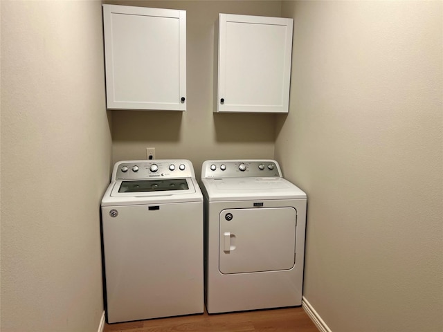 washroom featuring cabinets, washing machine and dryer, and light wood-type flooring