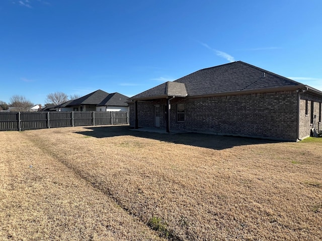 exterior space with roof with shingles, brick siding, a lawn, and fence