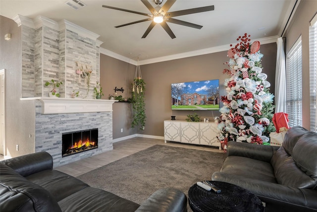 living room featuring light hardwood / wood-style flooring, a stone fireplace, ceiling fan, and crown molding