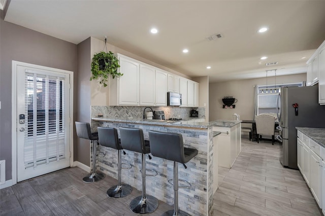 kitchen with kitchen peninsula, a breakfast bar, white cabinets, and appliances with stainless steel finishes