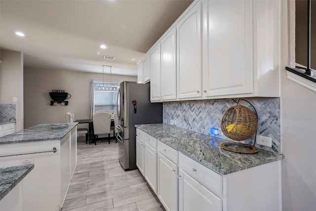 kitchen featuring stone counters, tasteful backsplash, stainless steel fridge, decorative light fixtures, and white cabinets