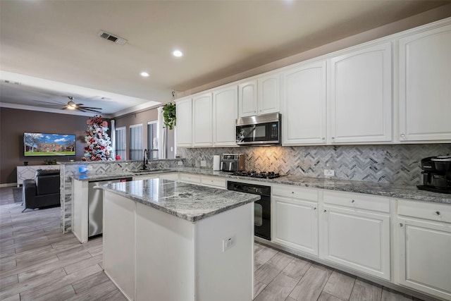 kitchen featuring appliances with stainless steel finishes, light stone counters, ceiling fan, sink, and a kitchen island