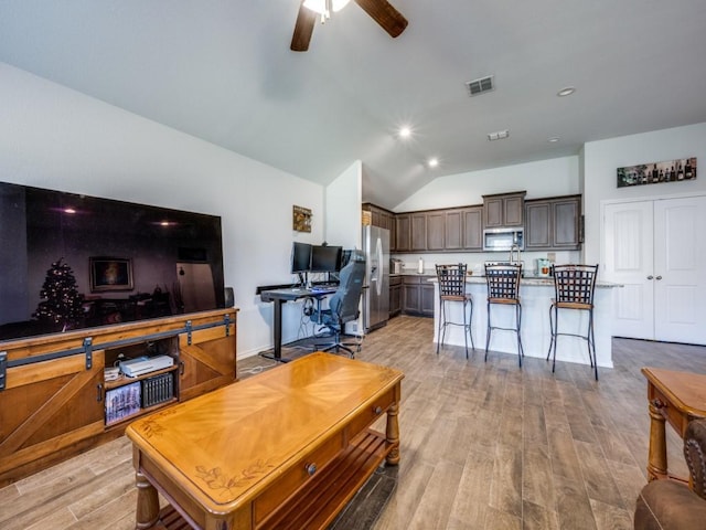 living room with vaulted ceiling, ceiling fan, and light wood-type flooring