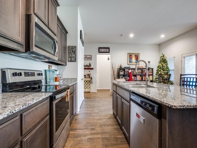 kitchen with hardwood / wood-style floors, a kitchen island with sink, sink, light stone counters, and stainless steel appliances