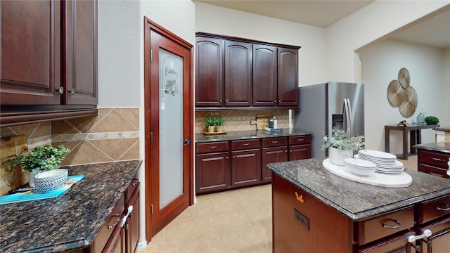 kitchen with tasteful backsplash, dark stone countertops, stainless steel fridge, and a center island