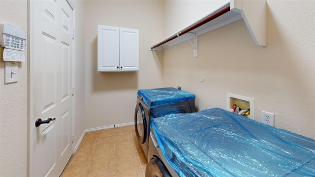 clothes washing area with cabinets, washer / dryer, and light tile patterned floors