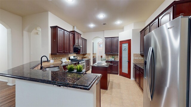 kitchen with backsplash, dark stone counters, sink, appliances with stainless steel finishes, and kitchen peninsula