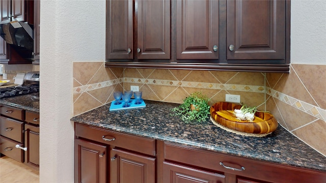 kitchen featuring stainless steel range, decorative backsplash, dark stone counters, and exhaust hood