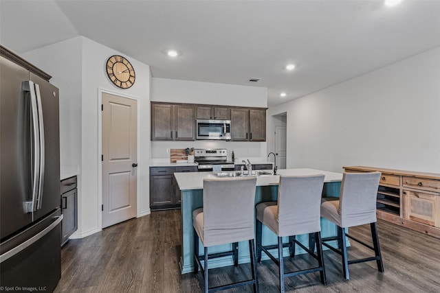 kitchen with dark brown cabinets, a kitchen breakfast bar, stainless steel appliances, dark hardwood / wood-style floors, and a center island with sink