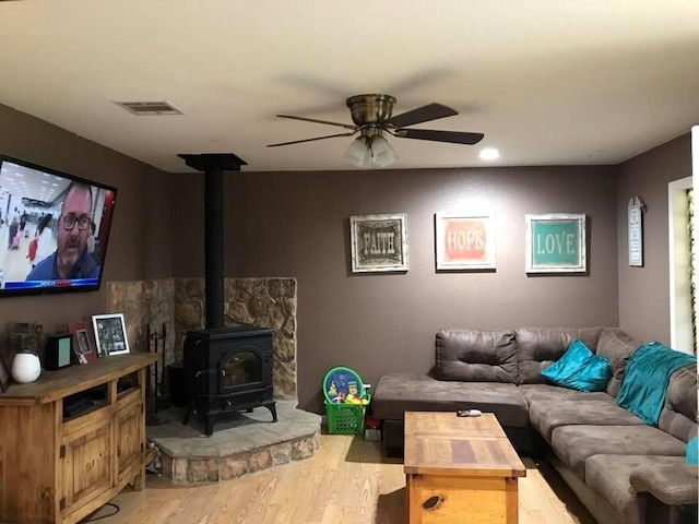 living room featuring a wood stove, ceiling fan, and light hardwood / wood-style floors