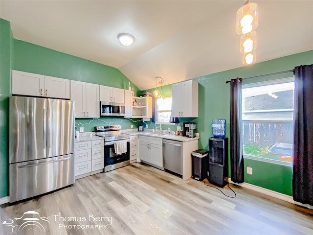 kitchen with pendant lighting, vaulted ceiling, stainless steel appliances, and white cabinetry