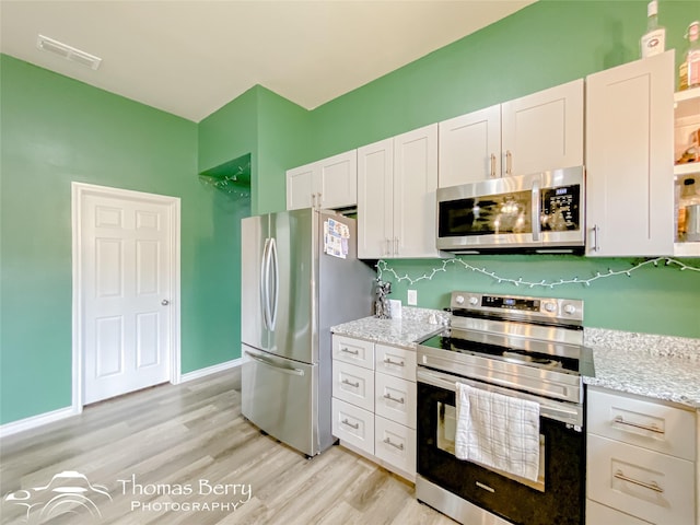 kitchen featuring light stone countertops, white cabinets, light wood-type flooring, and appliances with stainless steel finishes