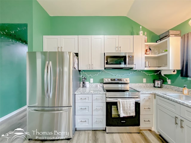 kitchen featuring light stone countertops, stainless steel appliances, light hardwood / wood-style flooring, white cabinets, and lofted ceiling